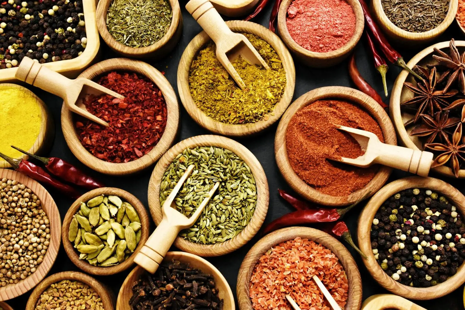 Assorted spices in wooden bowls with scoops.